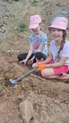 Uśmiechnięte dziewczynki siedzące na ziemi trzymają młotki i pędzle.