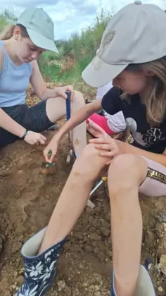 Dziewczyny w czapkach, siedząc na ziemi pędzelkami czyszczą podłoże.