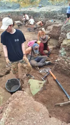 Studenci szukają skamieniałości siedząc przed ścianą ziemi.