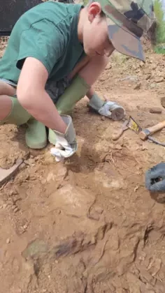 Chłopak w kaloszach i czapce i rękawicach kucając robi dziurę w ziemi.