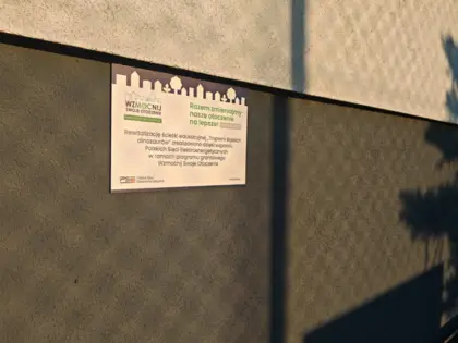 Tabliczka na ścianie budynku z informacją o dofinansowaniu w ramach Programu WzMOCnij swoje otoczenie.