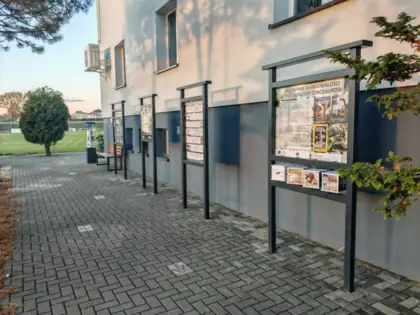 Pod ścianą budynku stoją tablice interaktywne.